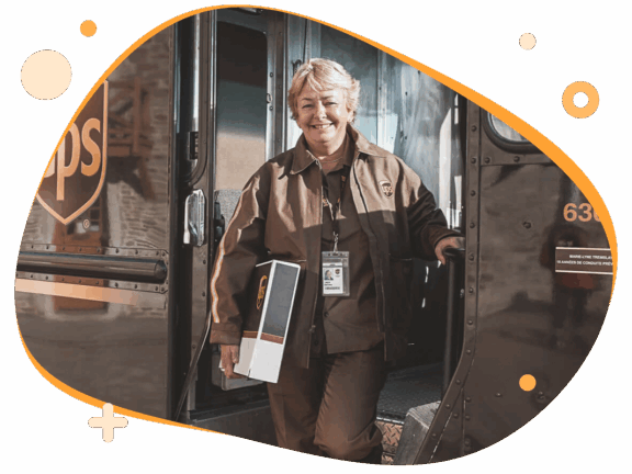 Bezorgster van UPS met een pakketje in haar hand. Ze staat in de deuropening van haar bus en lacht vrolijk.